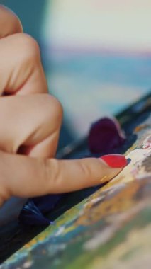 Ressamın kadın ellerine ve ressamların paletlerine yakından bakınca ressam, paletin üzerindeki parmaklarla boyaları karıştırıyor. Boyadaki ıslak parmak. Yaz, açık hava