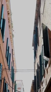 Kameranın genişliği Venedik 'in dar sokakları boyunca, iki katlı evler arasında, gökyüzüne bakan.