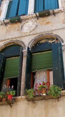 Venedik 'in eski ve güzel mimarisi, sıcak bir yaz gününde, mavi gökyüzüne karşı eski yeşil kepenkleri ve çiçekleri olan bir ev.,