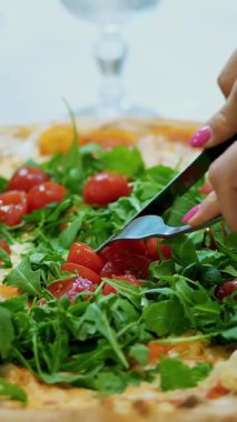 yakın çekim, büyük sulu, sıcak pizza Yeşiller, roka ve domates. Pizza bıçak ve çatal ile kesilmiş eller