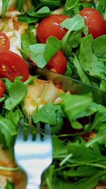 yakın çekim, büyük sulu, sıcak pizza Yeşiller, roka ve domates. Pizza bıçak ve çatal ile kesilmiş eller