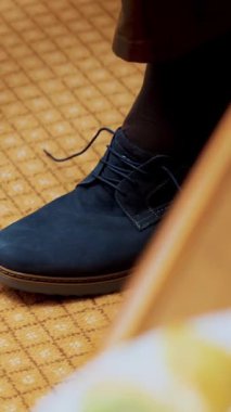 Yakın plan, erkek eli ayakkabı bağcığı. Adam şık mavi süet ayakkabılarını giyiyor, halı arka planında. Damat düğüne hazırlanıyor.