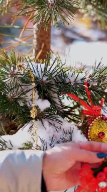 yakın çekim, bir kadın açık havada Noel süslemeleri ile Noel ağacı süsle. Noel oyuncaklar karla kaplı ağaç dalına asılı. kış, soğuk, karlı, güneşli bir gün.