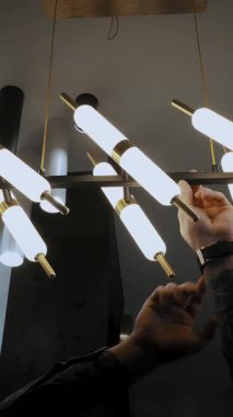 Dükkanda avizeler. Depoda şık lambalarla bir adam moda avizesi gösteriyor. İç tasarım için geniş bir aydınlatma yelpazesi.