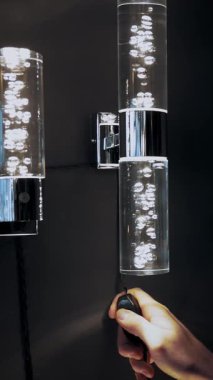 Avizeler mağazada. Yakın plan. İnsanın eli, baloncuk şeklinde dekorları olan güzel cam duvarlı, parlak bir lambayı yakar. İç tasarım için çeşitli aydınlatma araçları.