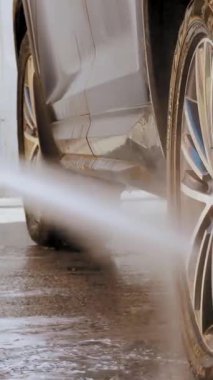 Araba yıkama. Yakın plan. Bir adam arabanın tekerleklerini yıkıyor, yüksek basınçlı temiz suyla, dışarıda, oto yıkamada. Araba Temizleme.