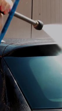 Araba yıkama. Yakın plan. Bir adam arabanın arka camını yıkıyor, temiz su, yüksek basınç spreyi ile, dışarıda, oto yıkamada. Araba Temizleme.