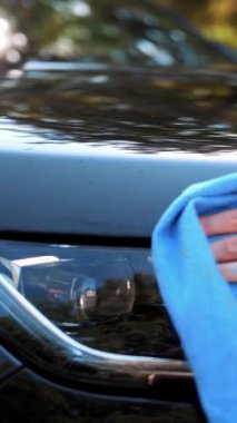 Araba yıkama, araba silme. Yakın plan. Kadın dışarıda bir bez parçasıyla otomobili siliyor, yıkandıktan sonra, oto yıkamada. Araba Temizleme.