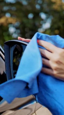 Araba yıkama, araba silme. Yakın plan. Kadın bir otomobili siliyor, bir bez parçasıyla dikiz aynasıyla, dışarıda, yıkamadan sonra, oto yıkamada. Araba Temizleme.