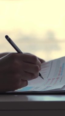 yakın çekim, kadın el, siyah kalem tutan ve bir şeyler yazıyor belgeleri, grafikleri ve diyagramları, beyaz bir masaüstü ofis ile çalışan iş kadın