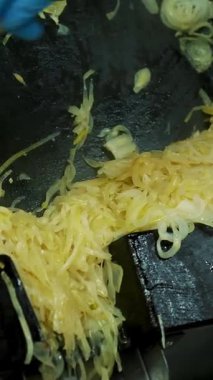 Yakın planda, eldivenli bir aşçı büyük endüstriyel kızartma tavasından bol miktarda kızarmış soğan döker. Yemekhanede, restoranda yemek pişirme süreci. Kızarmış soğan, kızarmış soğan.