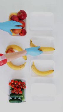 Üst Manzara. Koruyucu eldivenlerdeki gönüllüler bakkal paketleri, meyve ve sebzeleri tepsilere koyup kapatıyorlar. Coronavirus sırasında yemek servisi ve paket servisi. İnternetten alışveriş.