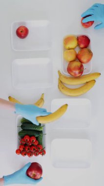 Üst Manzara. Koruyucu eldivenlerdeki gönüllüler bakkal paketleri, meyve ve sebzeleri tepsilere koyup kapatıyorlar. Coronavirus sırasında yemek servisi ve paket servisi. İnternetten alışveriş.