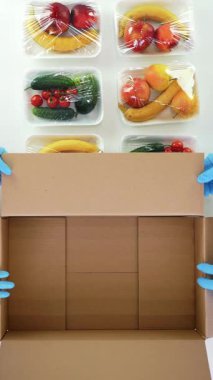 Üst Manzara. Koruyucu eldivenlerdeki gönüllüler bakkal paketleri, meyve ve sebzeleri tepsilere koyup kapatıyorlar. Coronavirus sırasında yemek servisi ve paket servisi. İnternetten alışveriş.