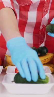 Üst Manzara. Koruyucu eldivenlerdeki gönüllüler bakkal paketleri, meyve ve sebzeleri tepsilere koyup kapatıyorlar. Coronavirus sırasında yemek servisi ve paket servisi. İnternetten alışveriş.