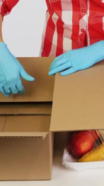 Üst Manzara. Koruyucu eldivenlerdeki gönüllüler bakkal paketleri, meyve ve sebzeleri tepsilere koyup kapatıyorlar. Coronavirus sırasında yemek servisi ve paket servisi. İnternetten alışveriş.