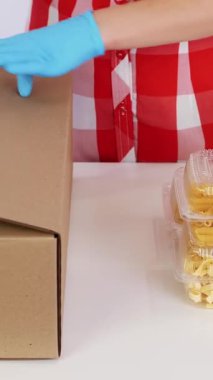 Üst Manzara. Koruyucu eldivenlerdeki gönüllüler bakkal paketleri, meyve ve sebzeleri tepsilere koyup kapatıyorlar. Coronavirus sırasında yemek servisi ve paket servisi. İnternetten alışveriş.