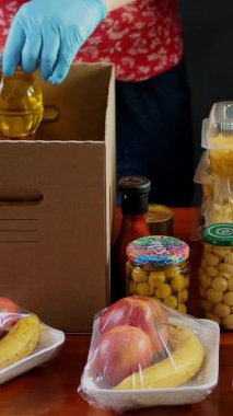 Yakın plan, koruyucu eldivenli gönüllüler marketi karton bağış kutularına dolduruyorlar. Coronavirus sırasında paket servis, kapı yemek servisi. İnternetten alışveriş. Hayırseverlik.