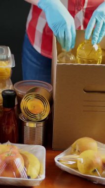 Yakın plan, koruyucu eldivenli gönüllüler marketi karton bağış kutularına dolduruyorlar. Coronavirus sırasında paket servis, kapı yemek servisi. İnternetten alışveriş. Hayırseverlik.