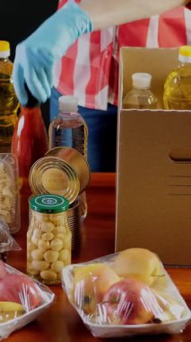Yakın plan, koruyucu eldivenli gönüllü marketten karton bağış kutusuna yiyecek paketliyor. Coronavirus sırasında paket servis, kapı yemek servisi. İnternetten alışveriş. Hayırseverlik.