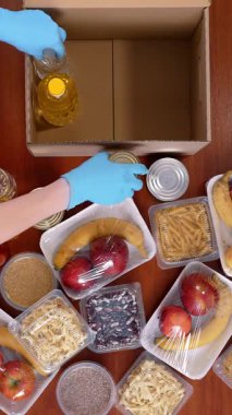 Üst düzey, yakın plan, koruyucu eldivenli gönüllü marketten karton bağış kutusuna yiyecek paketliyor. Coronavirus sırasında paket servis, kapı yemek servisi. İnternetten alışveriş. Hayırseverlik.