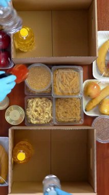 Üst düzey, yakın plan, koruyucu eldivenli gönüllüler marketi karton bağış kutularına dolduruyor. Coronavirus sırasında paket servis, kapı yemek servisi. İnternetten alışveriş. Hayırseverlik.