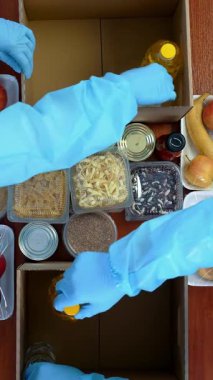 Üst düzey, yakın plan, koruyucu eldivenli gönüllüler, takım elbiseler karton bağış kutularına bakkal paketleri. Coronavirus sırasında paket servis, kapı yemek servisi. İnternetten alışveriş. Hayırseverlik.