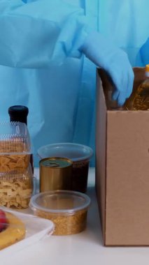 Koruyucu eldivenler içinde gönüllü, market alışverişini karton bağış kutusuna paketliyor. Coronavirus sırasında paket servis, kapı yemek servisi. İnternetten alışveriş. Hayırseverlik.