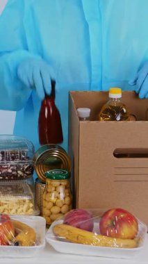 Koruyucu eldivenli gönüllü, takım elbiseli karton bağış kutularına market alışverişi yapıyor. Coronavirus sırasında paket servis, kapı yemek servisi. İnternetten alışveriş. Hayırseverlik.