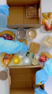 Üst düzey, yakın plan, koruyucu eldivenli gönüllüler, takım elbiseler karton bağış kutularına bakkal paketleri. Coronavirus sırasında paket servis, kapı yemek servisi. İnternetten alışveriş. Hayırseverlik.