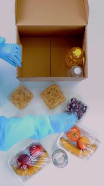 Koruyucu eldivenler içinde gönüllü, market alışverişini karton bağış kutularına paketliyor. Coronavirus sırasında paket servis, kapı yemek servisi. İnternetten alışveriş. Hayırseverlik.