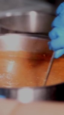 Yakın plan. Koruyucu eldiven giyen şef büyük bir tencereyle domates çorbası veya borş karıştırıyor. Sağlıklı yiyecekler, yemek pişirme, güvenlik kavramı. Matarayı yeniden aç