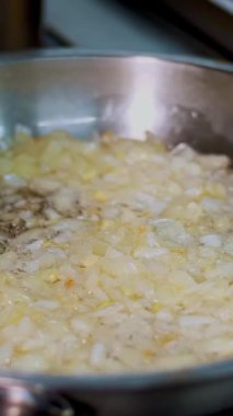 Yemek pişirmek. Yakın plan, kızartma tavasında kızarmış soğan. Aşçı koruyucu eldivenlerle soğanı karıştırıyor ve doğranmış havuçları ekliyor. Sağlıklı gıda ve güvenlik kavramı. Matarayı yeniden aç