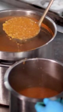 Yemek pişirmek. Yakın plan. Şef koruyucu eldivenlerle büyük bir tencereden küçük bir kaba sıcak portakal çorbası döker. Sağlıklı yemek. Gönüllü olmak ve yardım. Matarayı yeniden açıyorum. güvenlik kavramı.