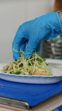 Yemek pişirmek. Yakın plan. Aşçı, koruyucu eldivenlerle, sebze salatasını küçük kaselere koyar ve tartıya göre tartır. Sağlıklı yemek. Gönüllü olmak ve yardım. Matarayı yeniden açıyorum. güvenlik kavramı.