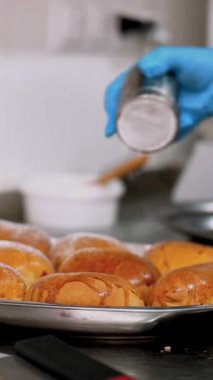 Yemek pişirmek. Fırın. Yakın plan. Fırıncı, koruyucu eldivenlerle, taze pişmiş hamur işlerinin üzerine şeker serpiyor. Sağlıklı yemek. Covid-19 'dan sonra tekrar açılıyor. Güvenlik kavramı. Gönüllülük ve yardım.