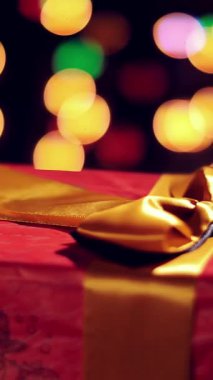 Altın kurdeleli güzel bir hediye. Bokeh ışıkları ya da parlak çelenk arka planında mevcut. Yakın çekim, rotasyon. Noel ya da yeni yıl. Yardım konsepti. Şenlikli atmosfer.