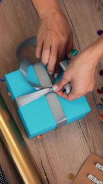 Hediyeler yakın çekimde paketleniyor. Üst Manzara. Hediye ve dekorasyon tasarımcısı bir hediye kutusu hazırlar, dizüstü bilgisayarın önüne ipek kurdeleyle fiyonk bağlar. video günlüğü, webinar.