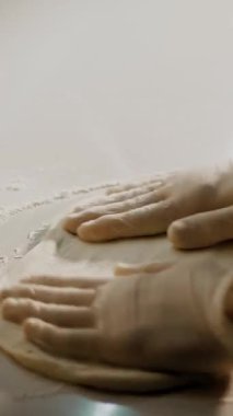 Yemek pişirme, fırın. Yakın plan. Şef, un serpiştirilmiş pizza hamurunu boş bir şekilde un masasına serper. Şef fırıncı elleri koruyucu eldiven giymiş..