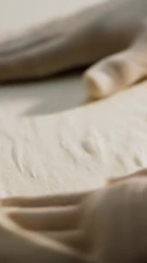 Yemek pişirme, fırın. Yakın plan. Şef, un serpiştirilmiş pizza hamurunu boş bir şekilde un masasına serper. Şef fırıncı elleri koruyucu eldiven giymiş.