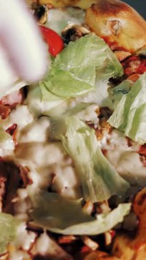 Aşçılık. Pizza yapmak. Yakın çekim, üst görüş. Şef taze pişmiş üzerine dilimlenmiş domatesli sıcak pizza serpiyor. İtalyan pizzası pişirme süreci