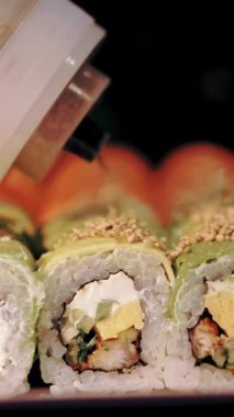 Geleneksel Japon yemekleri. Yakın plan. Yeni pişmiş, suşi bardan sipariş vermek için çeşitli suşi ruloları. Şef ekmeğe susam tohumu serpiyor.