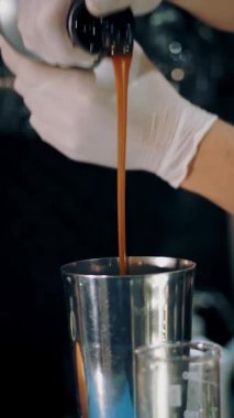 Barmen kokteyl yapar. Yakın plan. Barmen karamelli şurubu bir kokteyl karıştırıcısına dolduruyor. Barda, restoranda ya da diskoda..