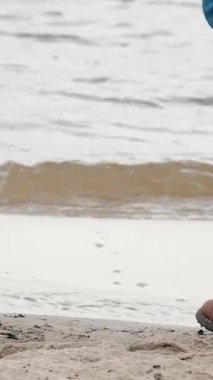 Kışın deniz kenarında yürüyorum. Yakın plan. Kahverengi çizmeli kadın gezgin, kumlu sahil ya da nehir kenarında yürüyor, rüzgarlı, soğuk, kış gününde. Kışın sahil boyunca yürü.