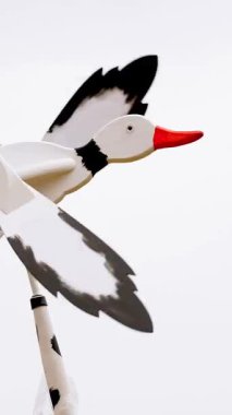 Rüzgar gülü. Komik, el yapımı, ahşap rüzgar gülü, uçan kaz ya da ördek şeklinde, rüzgarda dönüyor. Yakın plan. Beyaz gökyüzü arkaplanı