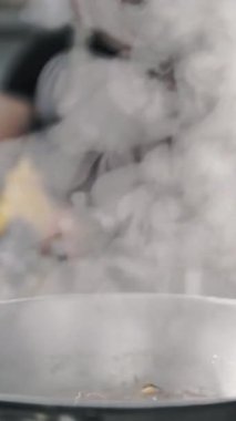 Yemek pişirmek. Buharda pişmiş. Açık büfe restoran mutfağı. Yakın plan. Yemek buharlaşıyor, tavada kaynıyor. Ticari bir mutfakta yemek hazırlamak ve pişirmek.