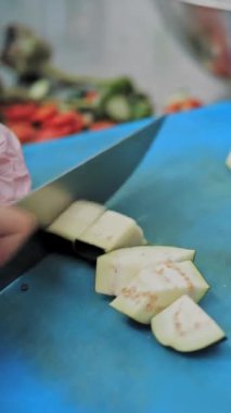 Yemek pişirmek. Şef sebze keser. Açık büfe restoran mutfağı. Yakın plan. Şef, plastik tahta üzerinde keskin, büyük mutfak bıçağıyla taze patlıcanları küçük parçalara ayırıyor..