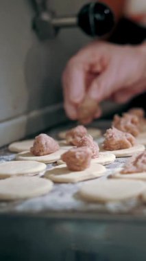 Yarı bitmiş ürünler. Yemek pişirmek. Yakın plan. Aşçının elleri hamur, mantı, ravioli ve pelmeni yapmak için hamur üzerine doğranmış et parçaları serer. Açık büfe restoran mutfağı..