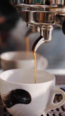 Kahve içeceğim. Yakın plan. Kahveci kahve makinesini kullanarak kahve hazırlar. İnce kahve akıntısı espresso makinesinden küçük beyaz bir fincana akar..