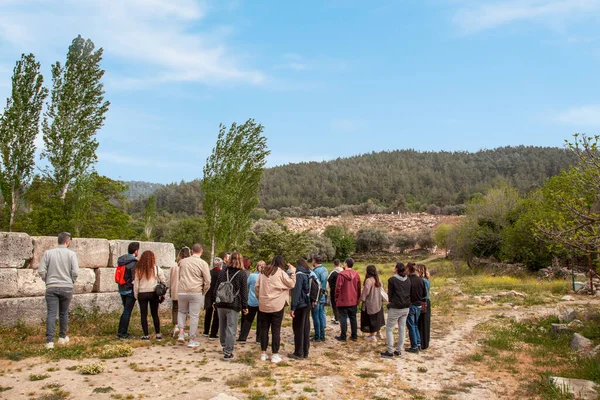 stock image Tourist group examines the ancient theater and historical artifacts in the open area. Mixed group of curious tourists, men and women.